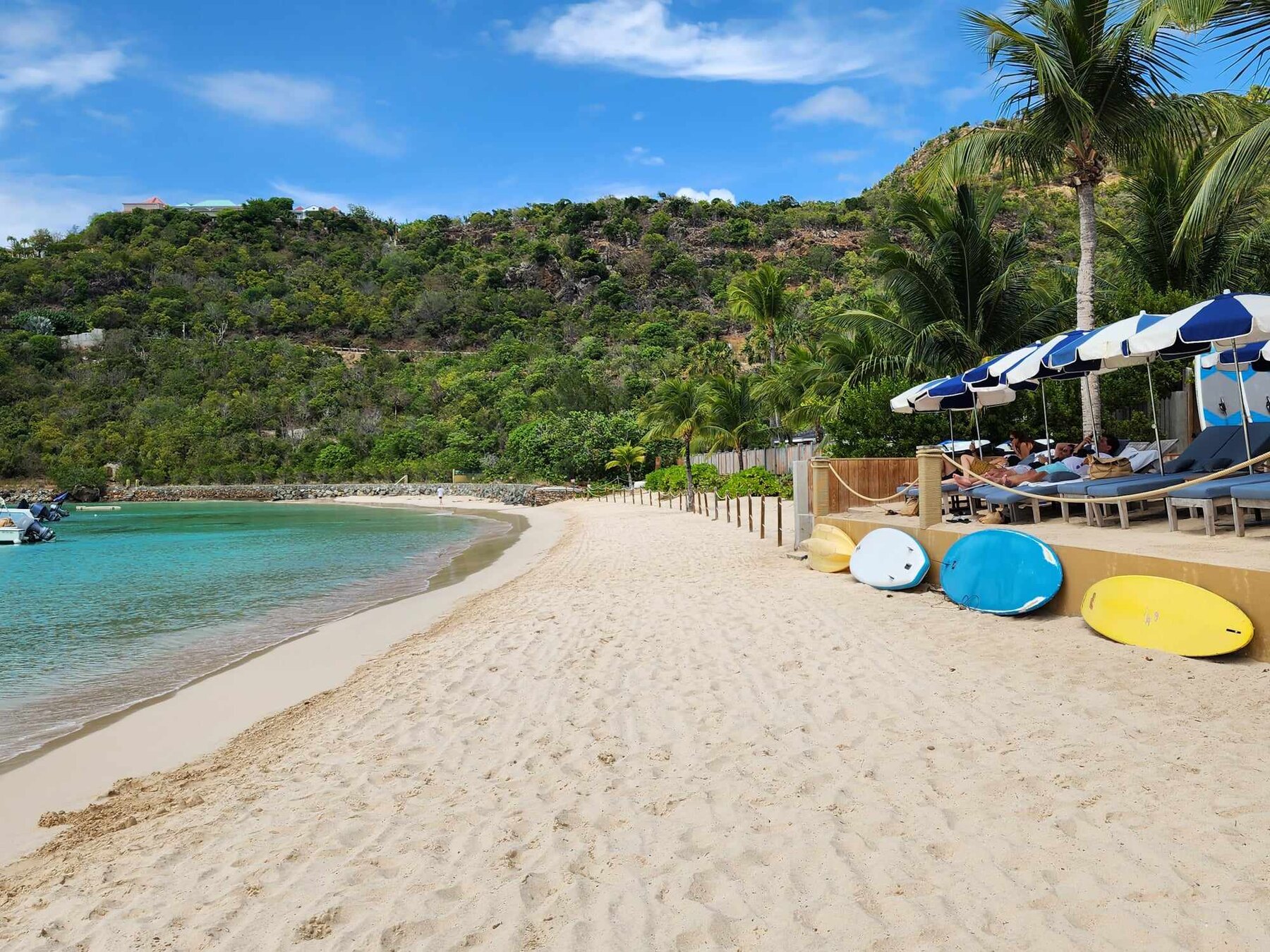 A turquoise St. Barth beach lined with palms and blue-and-white umbrellas